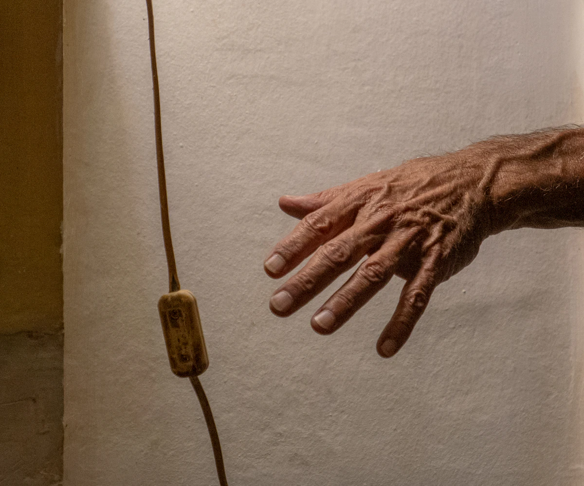 An older hand reaching for a light switch on a wall